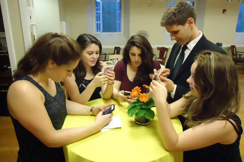 Group of young adults sitting around a table, each typing on a smartphone